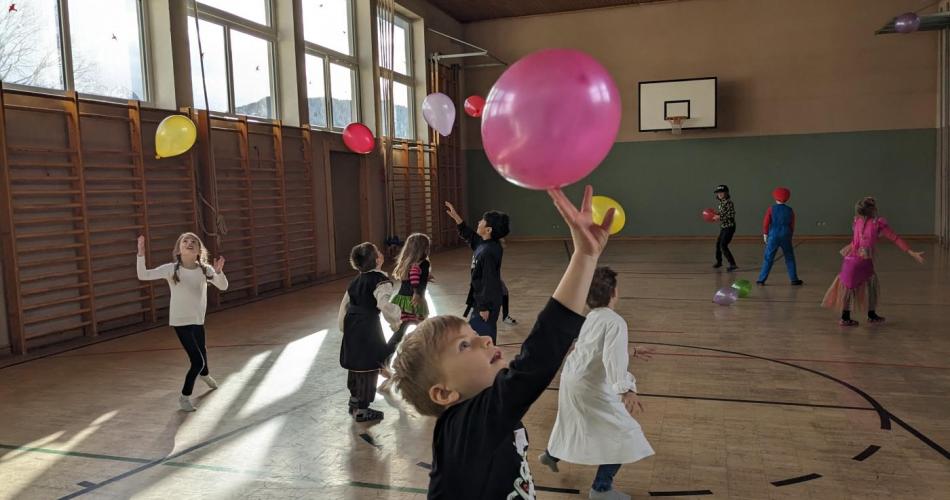 Turnsaal - verkleidete Kinder spilen mit Luftballons